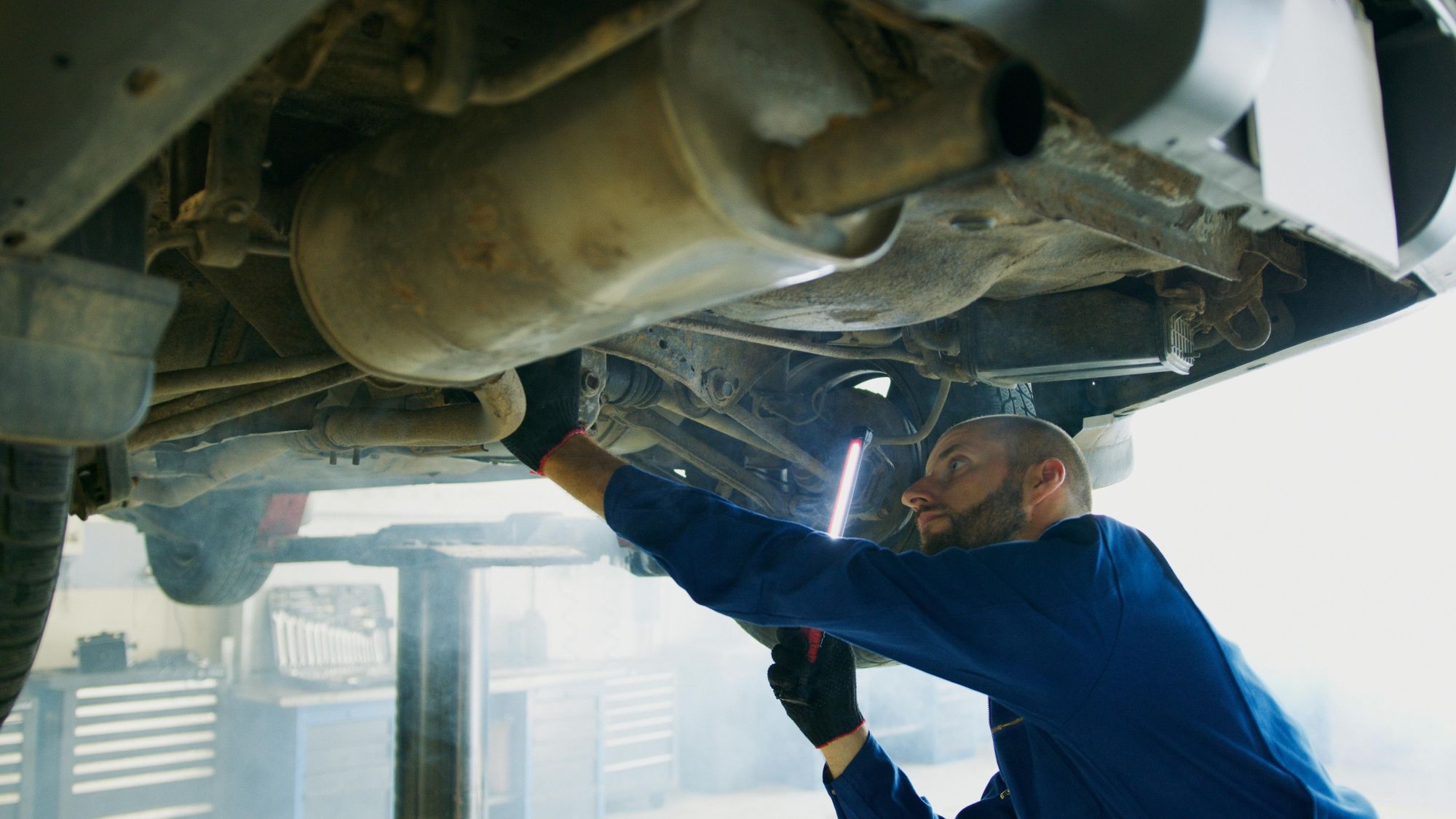 Monteur inspecteert met een lamp de onderkant van een voertuig in de werkplaats